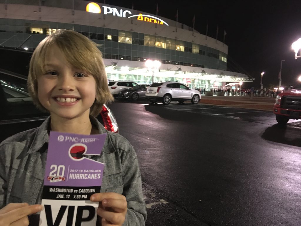 Boy smiles in front of PNC Arena holding up a VIP sign for the hockey game.