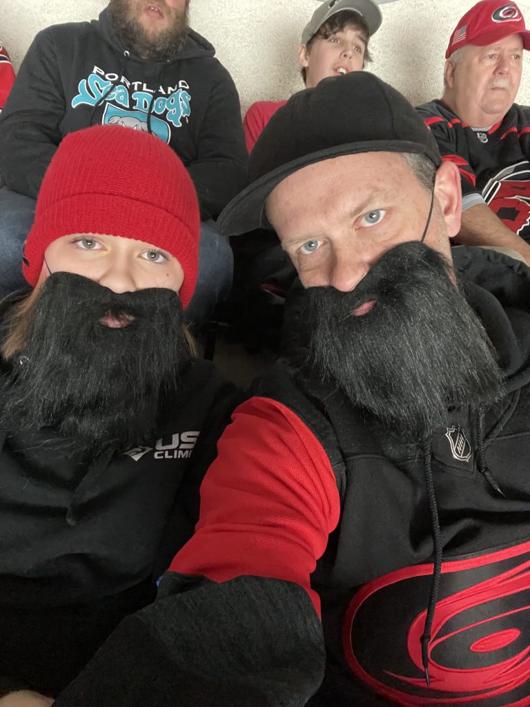 Two Hurricane's fans take a selfie wearing fake beards while sitting in the stands during a game.