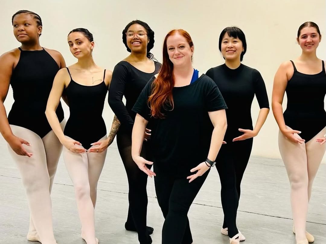 Six adult dancers stand in ballet pose while in the studio.