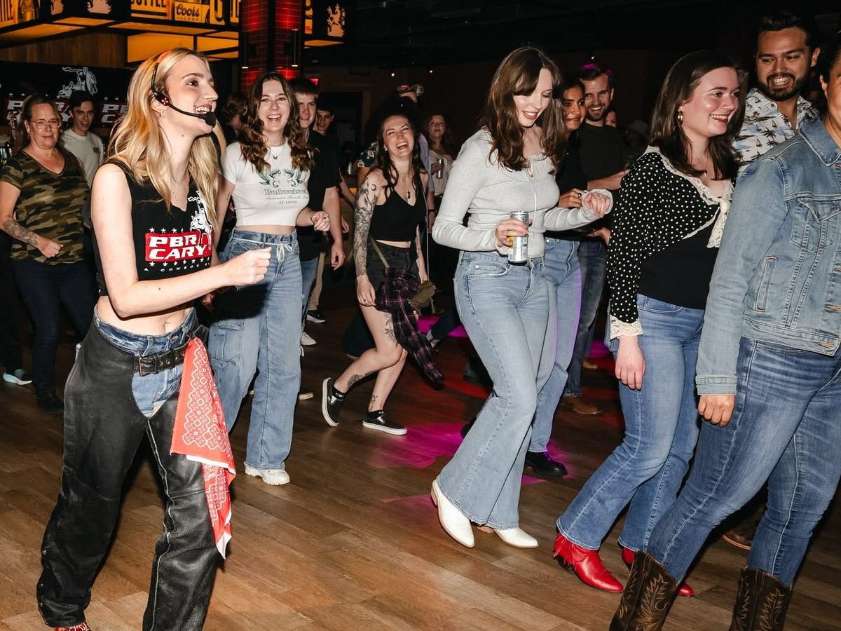 Dance instructor guides dancers in background in a line dancing lesson.