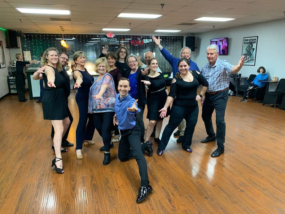 Group of adult dancers stretch their arms out toward the camera while in the dance studio.