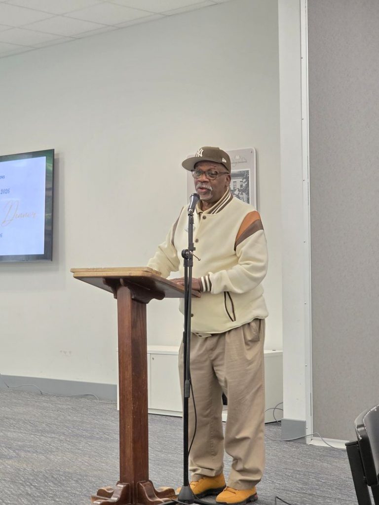 Man speaks into a microphone at the front of a room